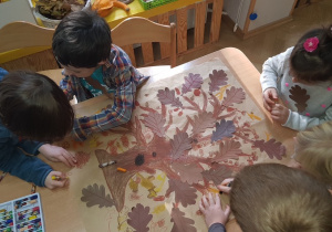 Dzieci przy stoliku przygotowują wspólnie plakat drzewa